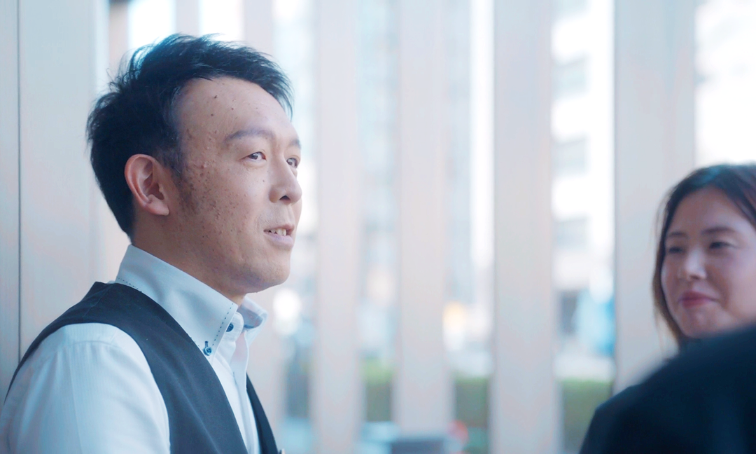 特徴3。ミライズを着用した男性が光が差し込む窓際で笑顔で外を見ている写真。